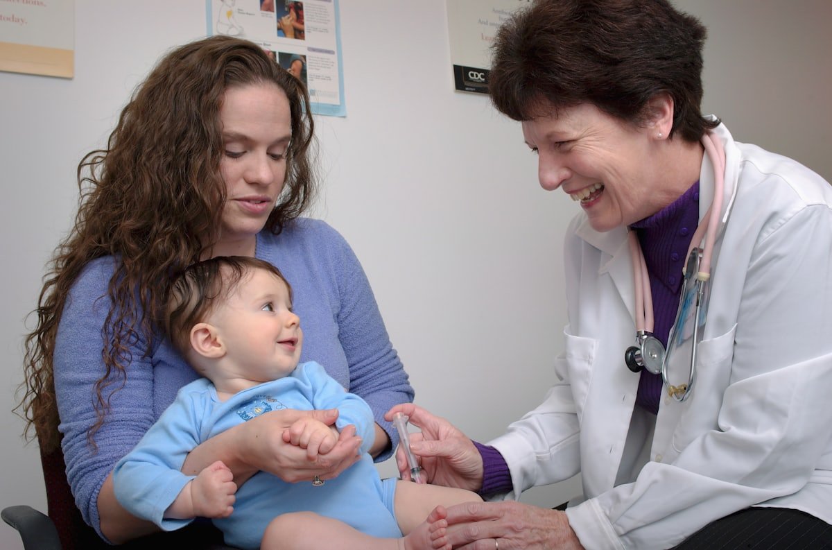 A pediatrician warmly examining a smiling baby held by a parent